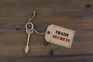 Key and a note on a wooden table with text - TRADE SECRETS